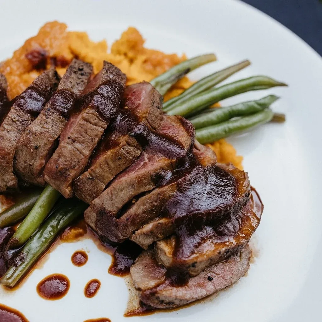Plated medium-rare steak, dark sauce, green beans, and orange puree.