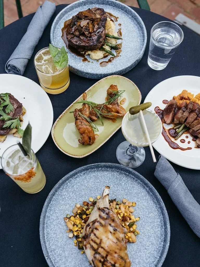 Top-down view: dark table displaying gourmet plated meat dishes and drinks.