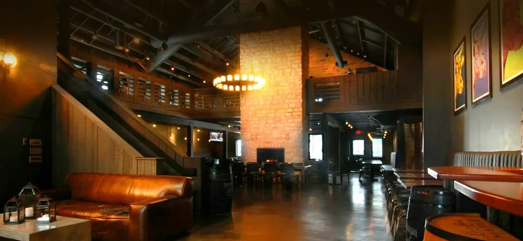 Warm-lit rustic-industrial restaurant with stone pillar, chandelier, and varied seating.