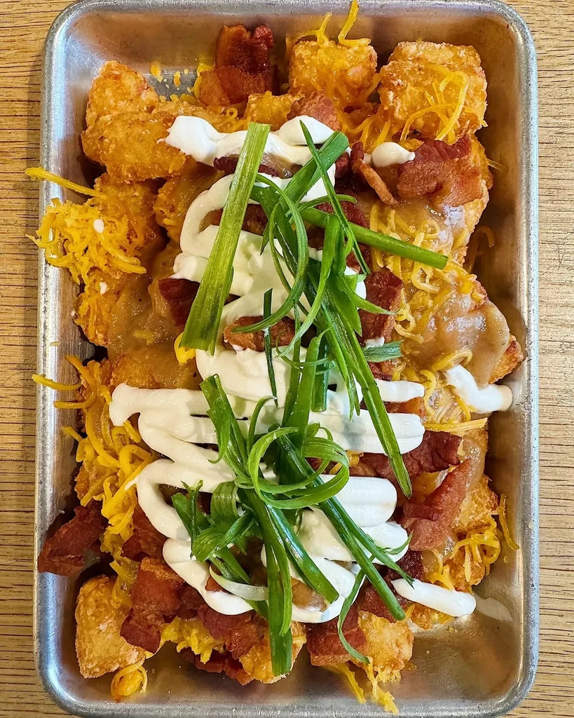 Crispy tater tots with melted cheese, bacon, sauces, and green onions.