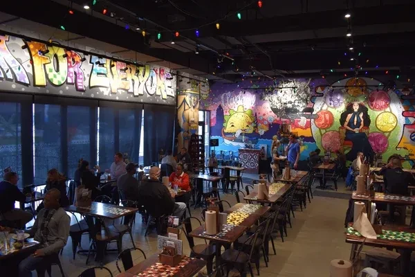 Vibrant restaurant interior featuring colorful graffiti murals, string lights, and diners.
