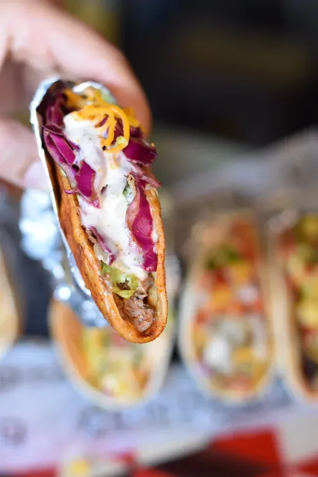Hand holding a loaded taco with meat, vegetables, sauce, and cheese.