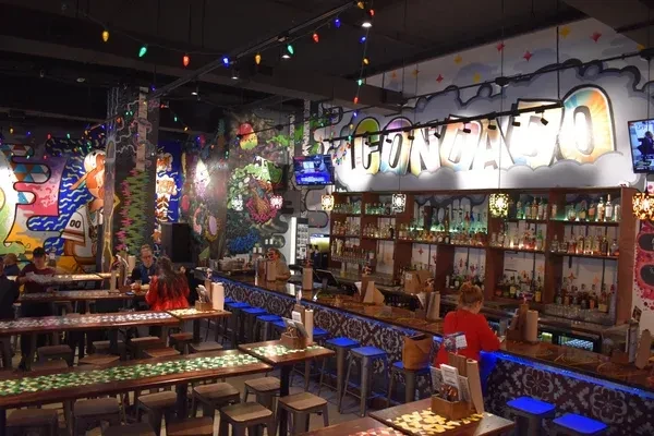 Interior of a colorful bar with 'CONGATO' mural, string lights, and guests.