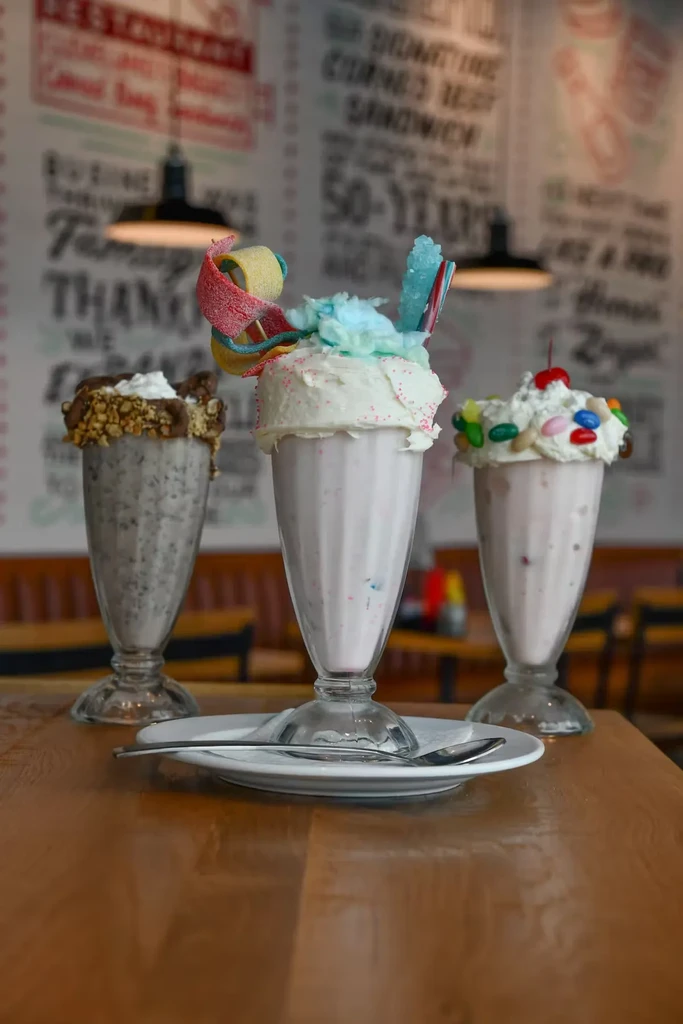 Three colorful, elaborate milkshakes with whipped cream and candy.