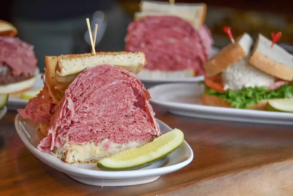 Generous pastrami on rye sandwich with sauerkraut and pickle.