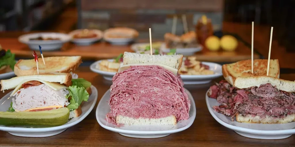 Three large deli sandwiches: club, tall pastrami, and roast beef.