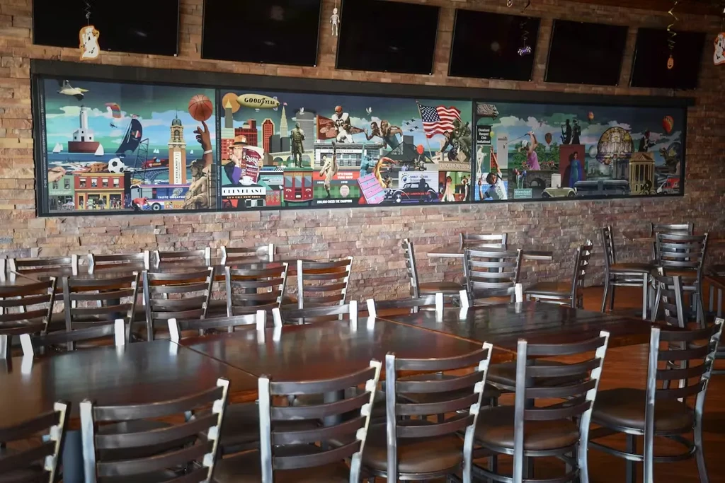 Empty restaurant dining area with wooden tables and Cleveland mural.