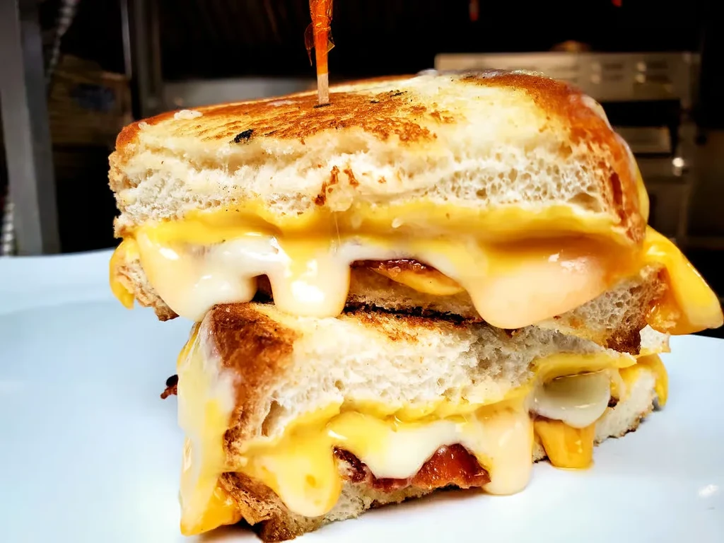 Stacked grilled cheese sandwich with melted cheese and visible bacon.
