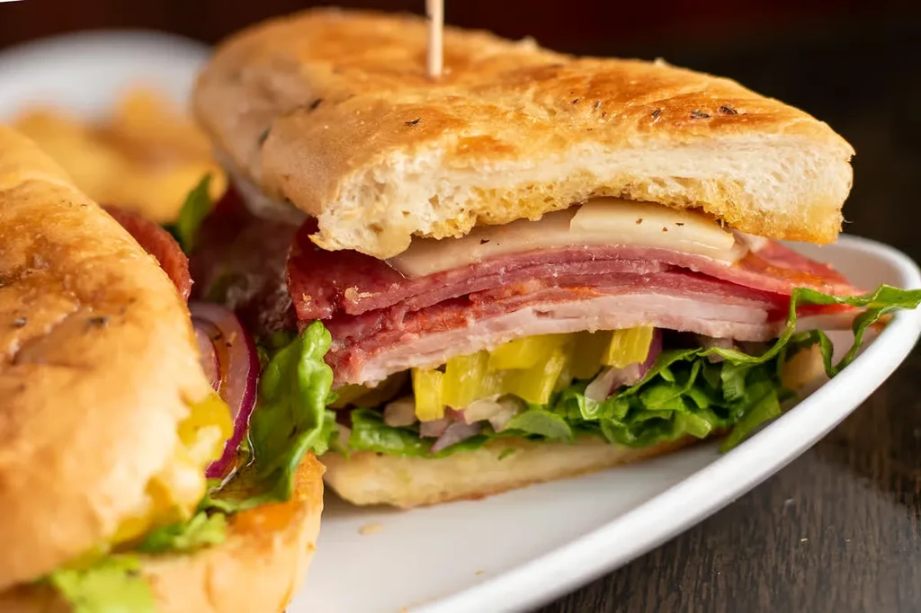 Sub sandwich cross-section with deli meats, cheese, lettuce, and pickled peppers.