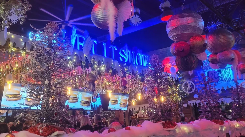 Festive restaurant interior with Christmas trees, "LET IT SNOW" sign, and burger ads.