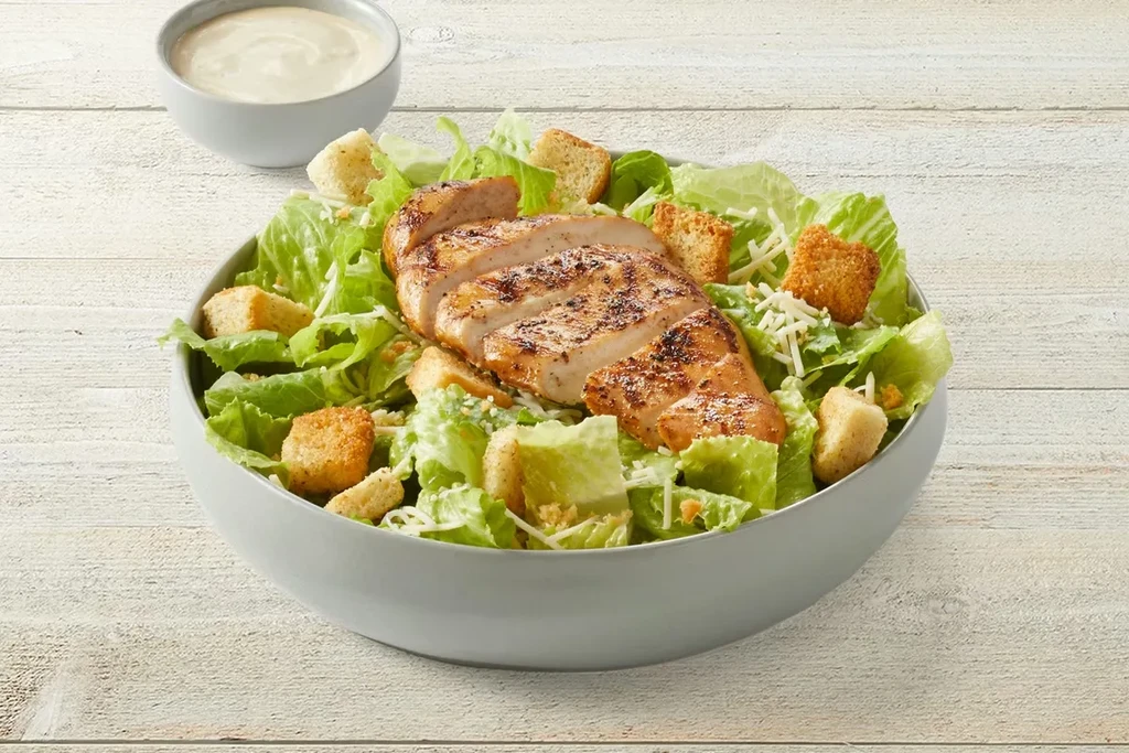 Grilled chicken Caesar salad in grey bowl on a wooden surface.