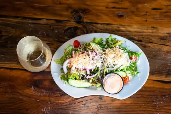 Fresh salad with mixed greens, cheese, dressing, and water on wood.