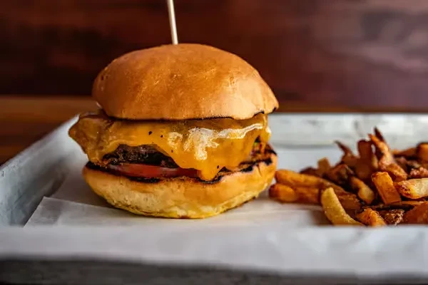 Close-up of a cheeseburger with melted cheese, tomato, and rustic fries.