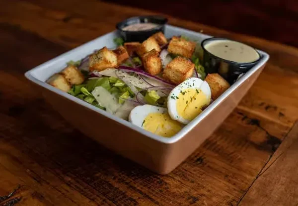 Fresh salad with lettuce, egg, croutons, cheese, and dressings on a wooden table.