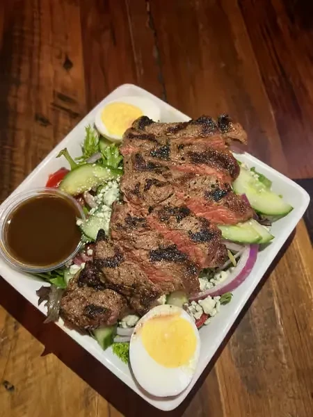 Grilled steak salad with egg, blue cheese, and side dressing.