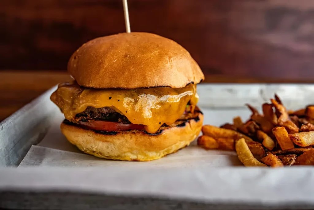 Close-up of a cheeseburger with melted cheese and fries.