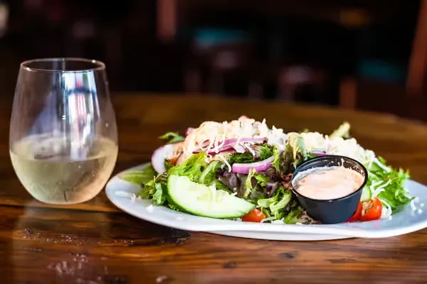 Close-up of fresh salad, white wine, pink dressing on dark wood.