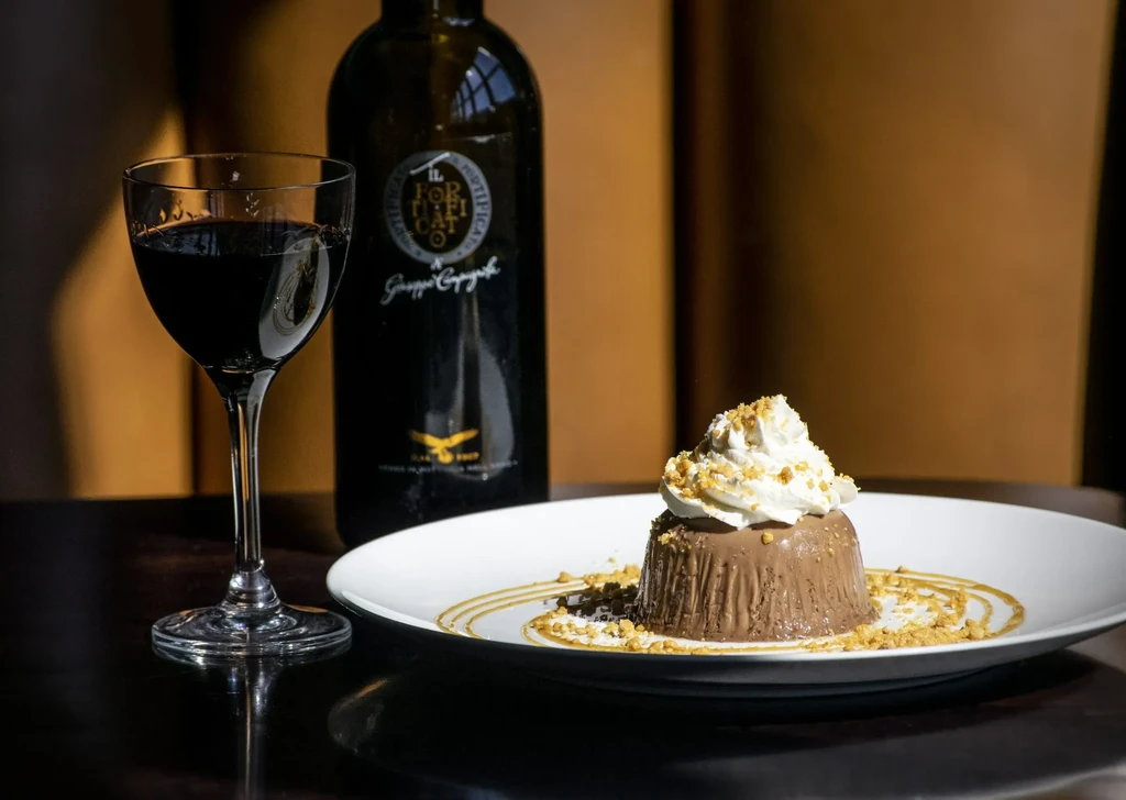 Professionally styled dark chocolate dessert, whipped cream, and red wine.