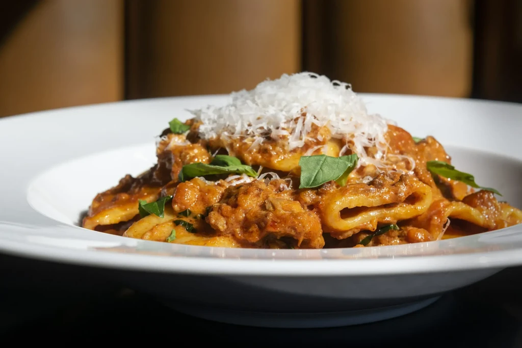 Tubular pasta with meat sauce, grated cheese, and fresh basil.