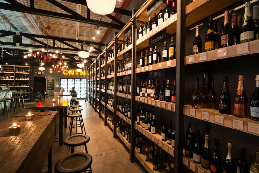 Wine bar: tall shelves of wine, communal tables, red chandelier.