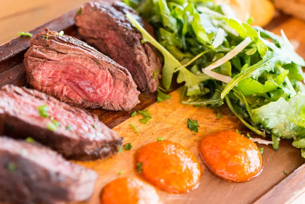 Medium-rare steak, arugula salad, and orange sauce on a cutting board.