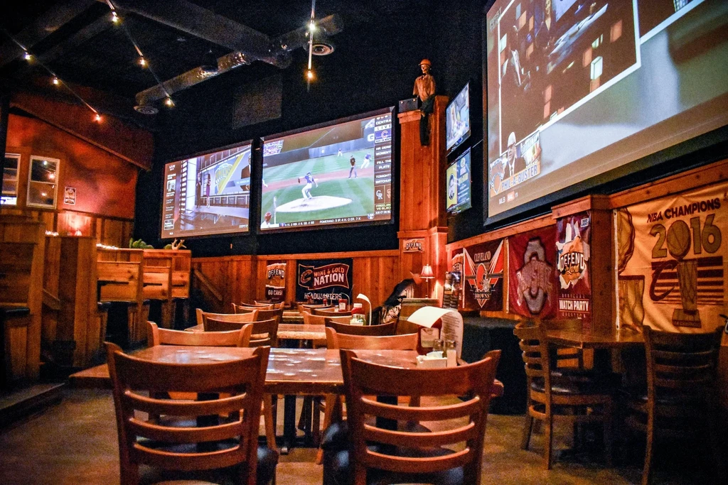 Dimly lit sports bar interior with TVs, banners, and wooden decor.