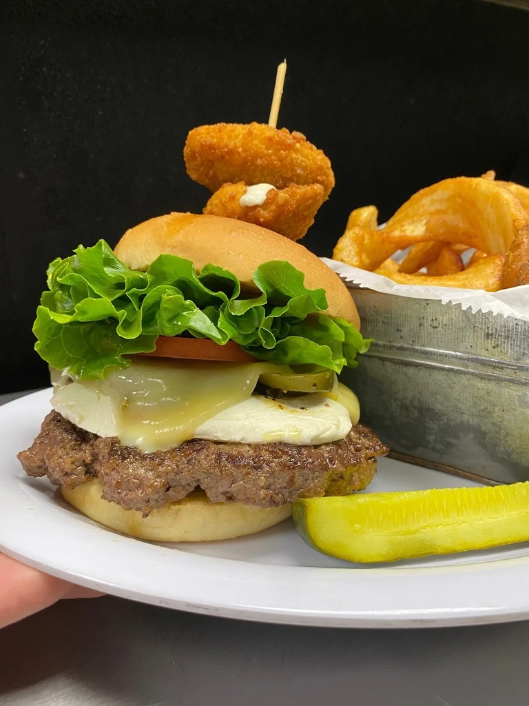 Hamburger with melted cheese, curly fries, and a pickle spear.