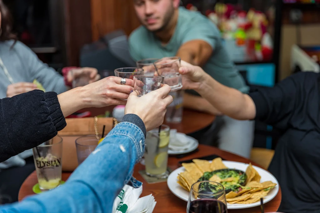 Hands toasting with glasses over a table of chips and dip.