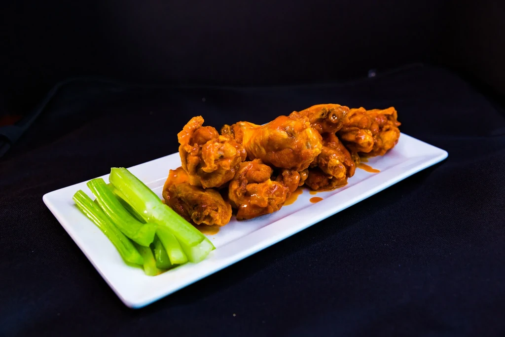 Buffalo chicken wings with sauce and celery on a white plate.