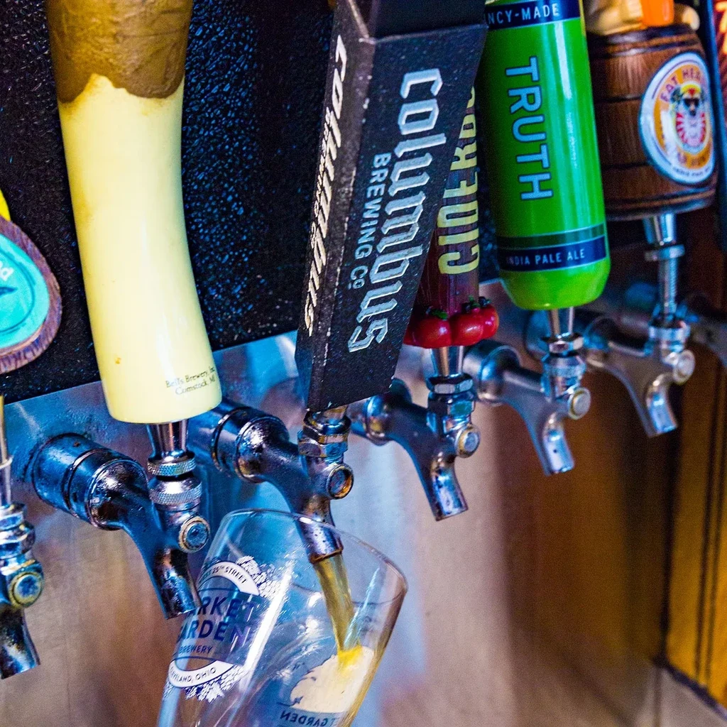 Close-up of beer taps, one pouring golden beer into a branded glass.