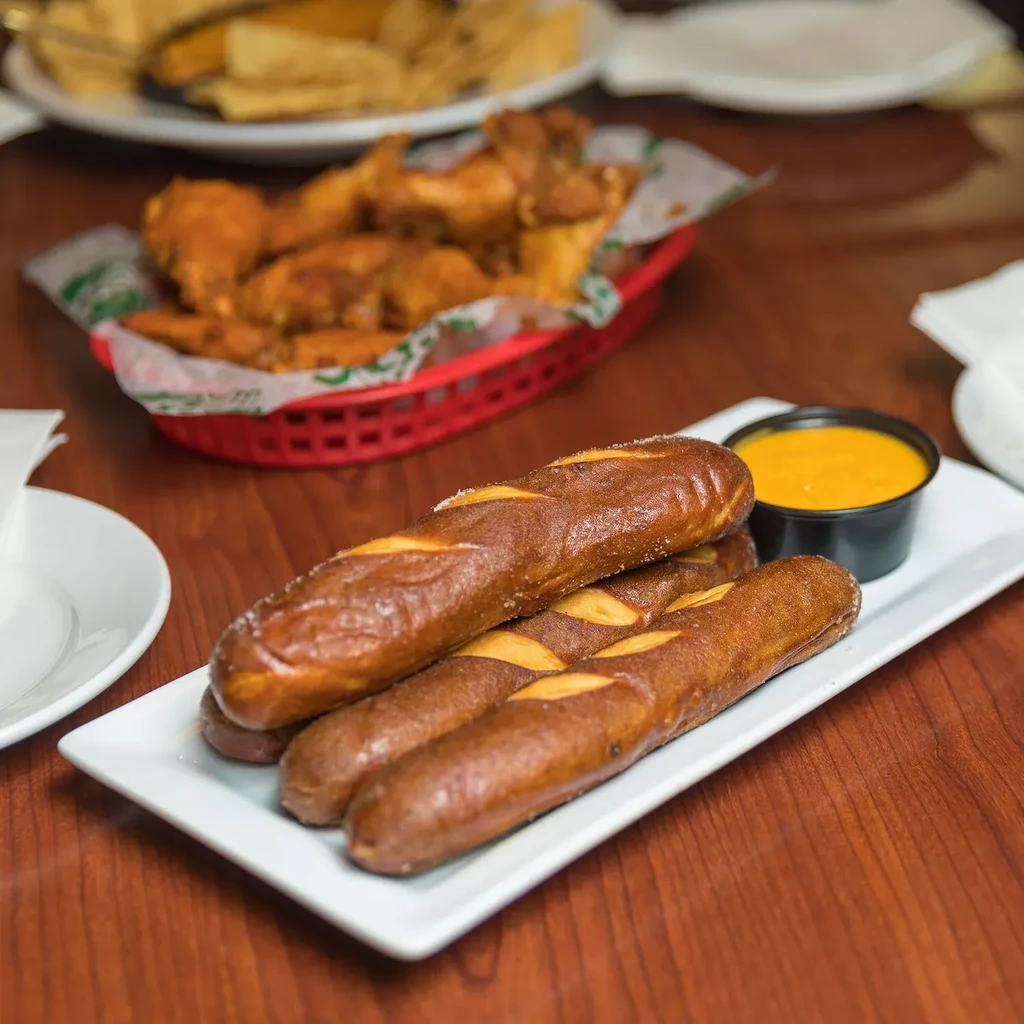 Golden-brown pretzel sticks with yellow dip on a plate, wooden table.