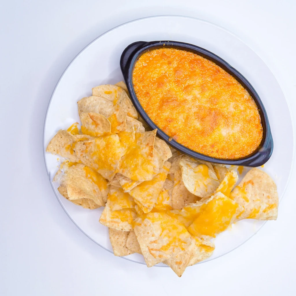 Hot cheese dip in ramekin with cheesy tortilla chips.