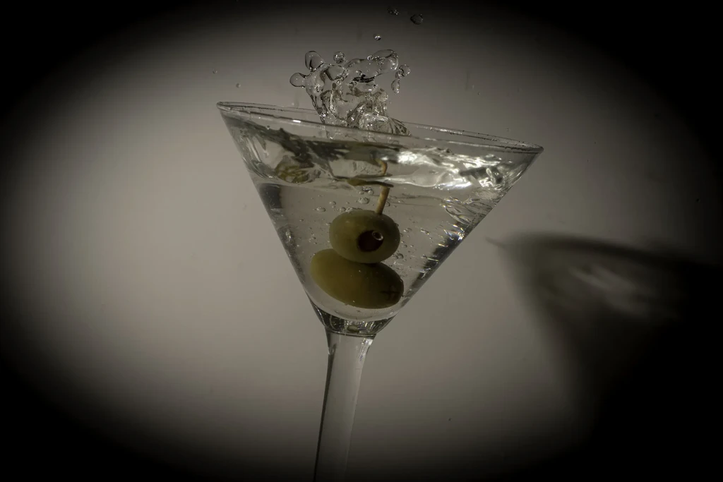 Martini glass with two olives on toothpick, dynamic splash, dark background.