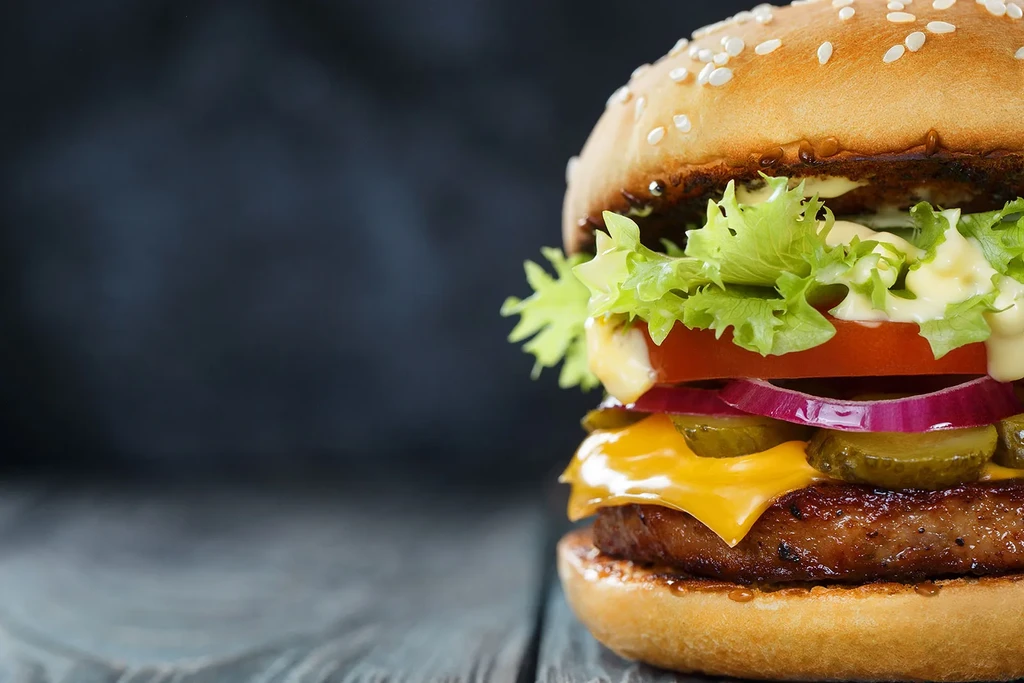 Gourmet burger with beef patty, melted cheese, fresh vegetables, sesame bun.