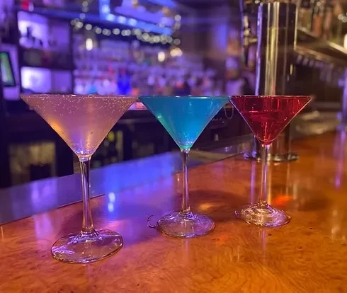 Three pale, blue, and red martini cocktails on a dimly lit bar.