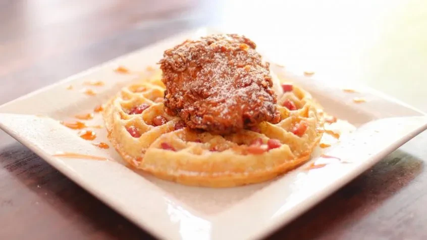 Crispy fried chicken, waffle, powdered sugar, and drizzled syrup.