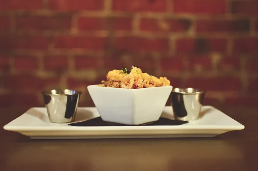 Fried calamari appetizer in a white bowl with two dipping sauces.