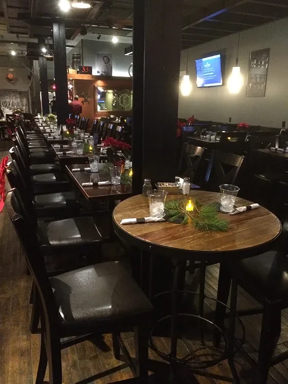 Dimly lit rustic restaurant interior with dark wooden tables and holiday decor.