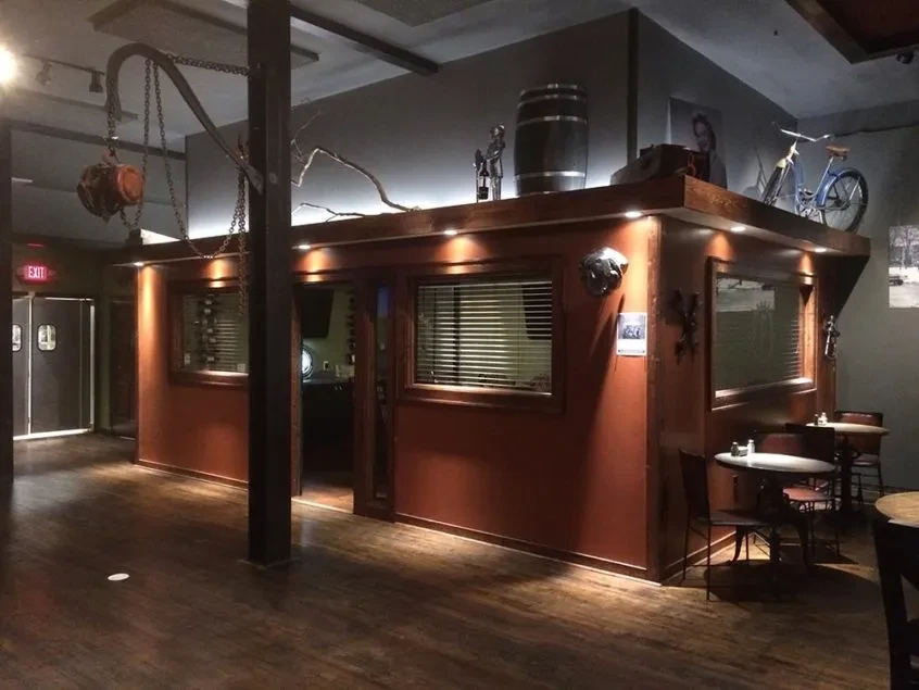 Dimly lit bar interior with wooden booth, vintage bicycle, and warm accents.
