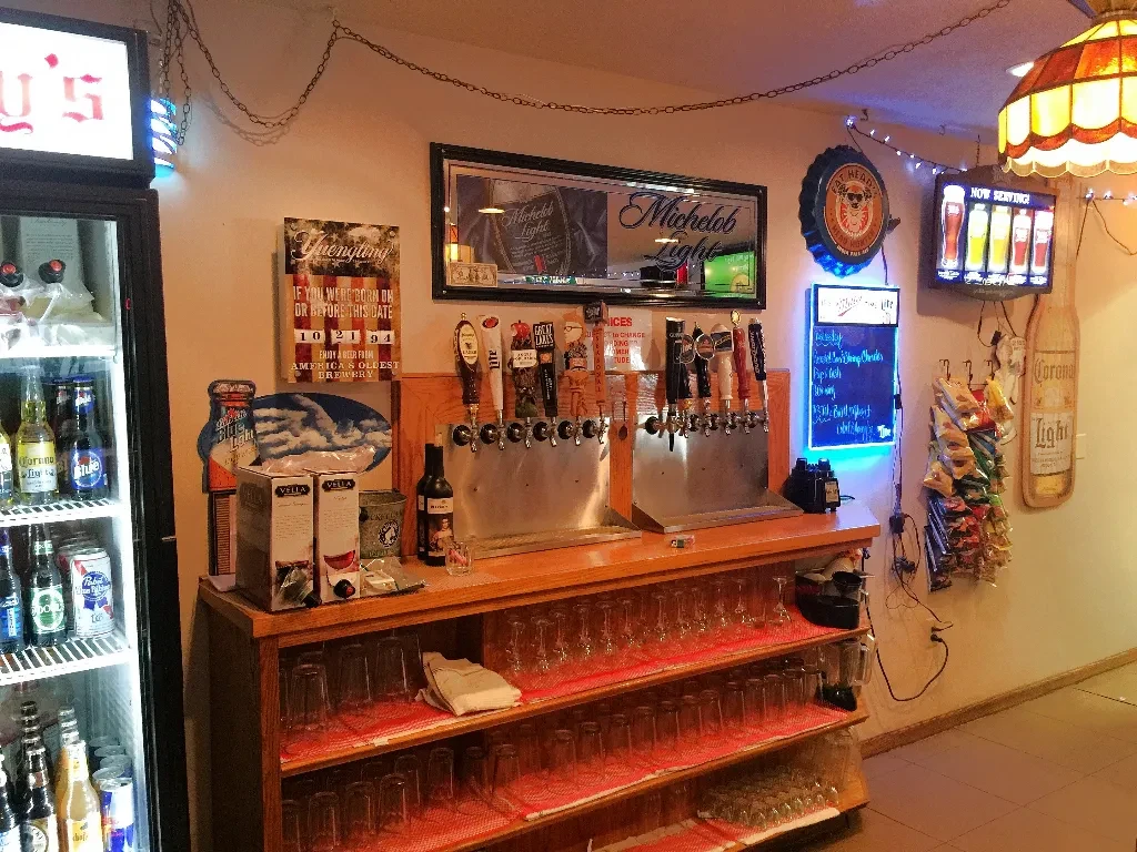 Bar interior featuring beer taps, stocked refrigerator, and various signs.