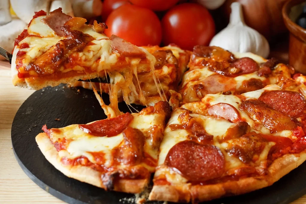 Pepperoni and sausage pizza with cheese pull on a dark serving board.
