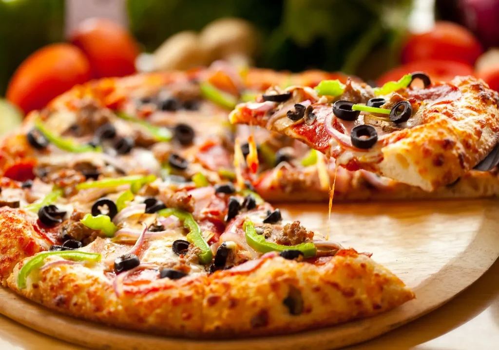 Supreme pizza on wooden peel, a cheesy slice being lifted.