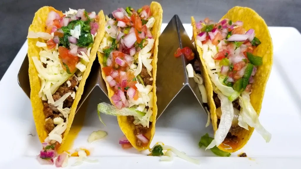 Three hard-shell tacos overflowing with beef, cheese, lettuce, and pico.