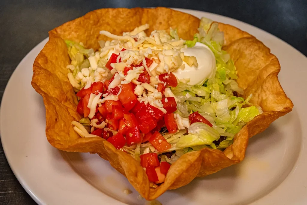 Taco salad in a crispy fried tortilla bowl with cheese and sour cream.
