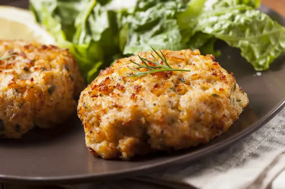 Two crispy, golden crab cakes with dill, lemon, and lettuce.