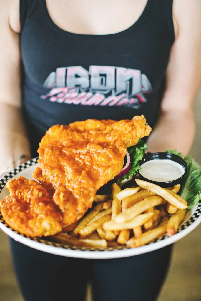 Plate of sauced chicken tenders and fries held by a person.