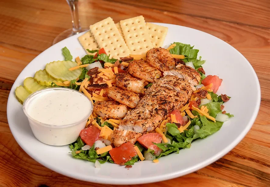 Large grilled chicken and shrimp salad with dressing and crackers.