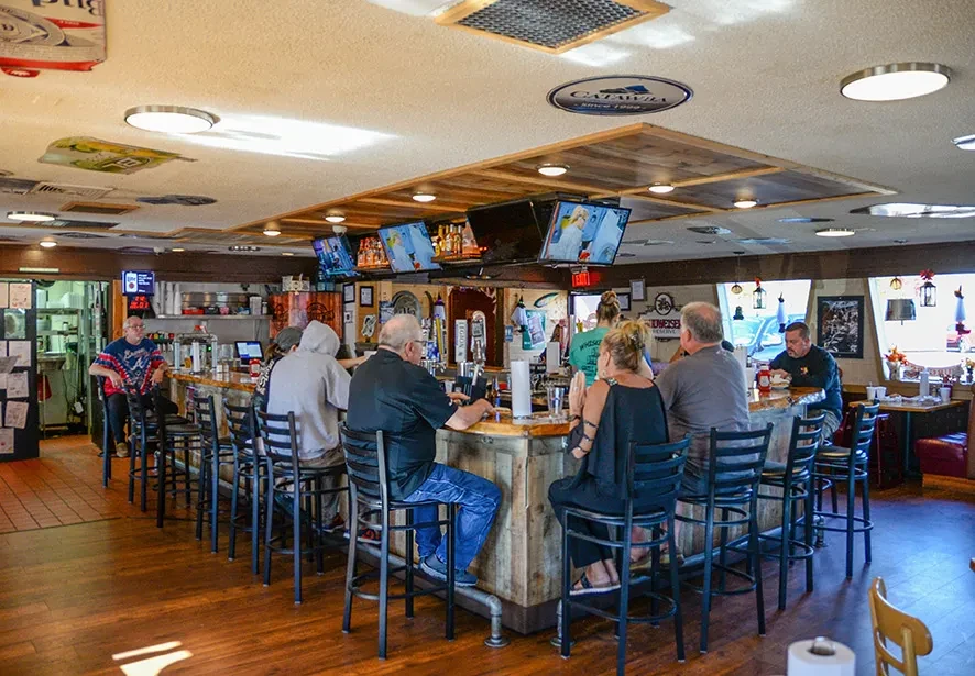 Busy casual bar interior with people, beer taps, and TVs.