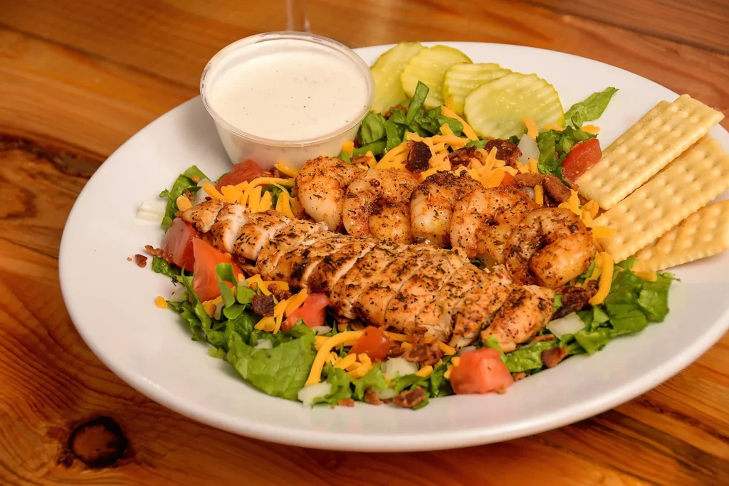 Grilled chicken and shrimp salad with dressing, pickles, and crackers.