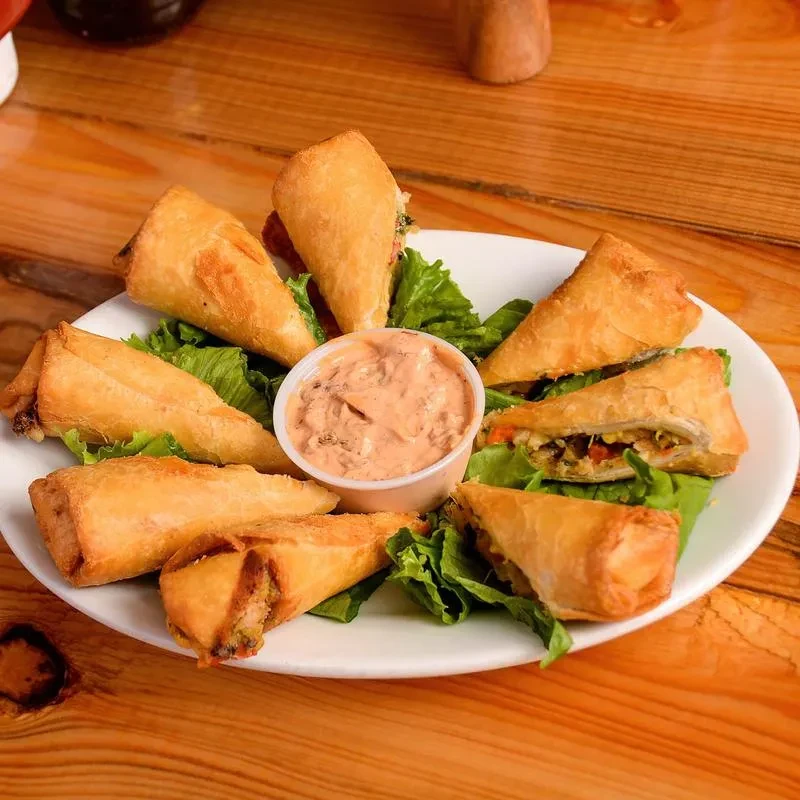 Close-up of fried vegetable appetizers, lettuce, and creamy dipping sauce.